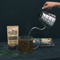 Tea being poured into a glass tea pot from a kettle with the Chai Walli Relax and Unwind product pack standing upright in the backdrop