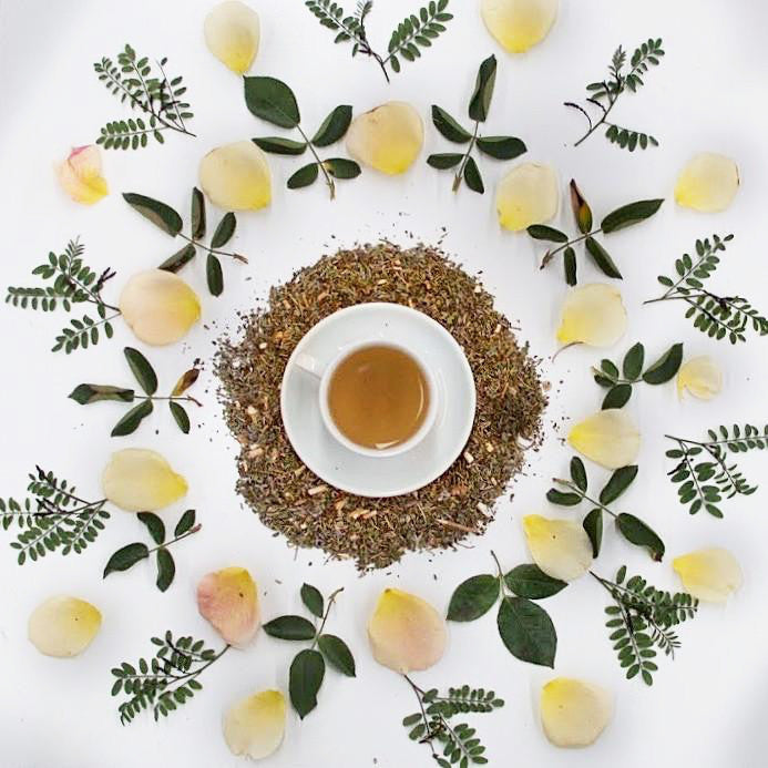 Top view of a white cup filled with the Relax and Unwind Tea on a white table decorated with rose petals and leaves