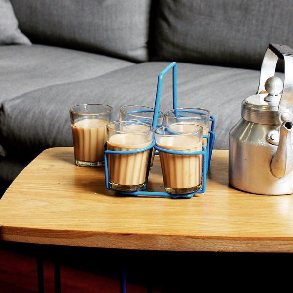 chai glasses with chai in a blue chai holder and a chai kettle on a table