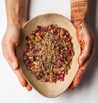 hands decorated in henna holding an oval dish containing the 11 spice chai caffeine free mix