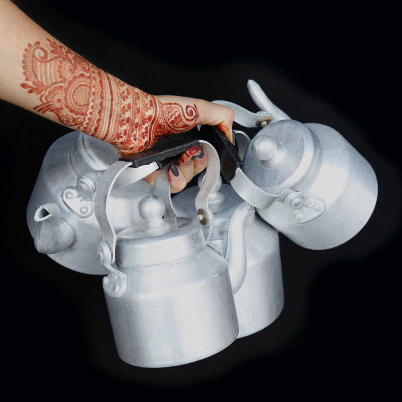a henna decorated hand holding four chai kettles